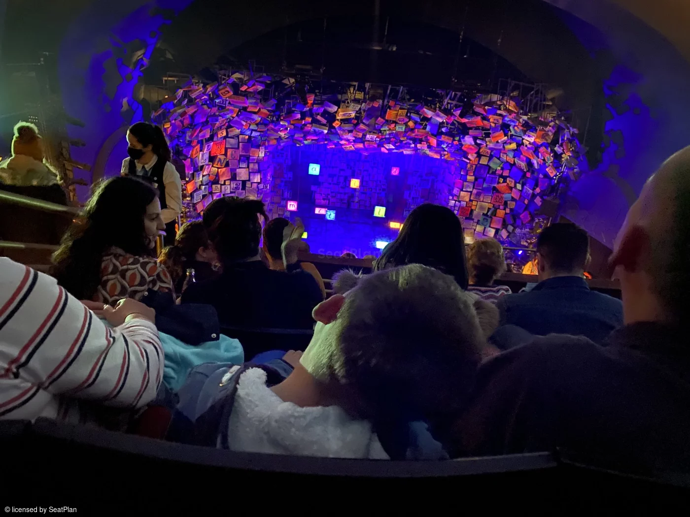 A seat view from the upper circle. It shows the colourful alphabet set, which spells out the word 'Matilda' in the centre of the stage. The view is slightly restricted by the audience members in front. 